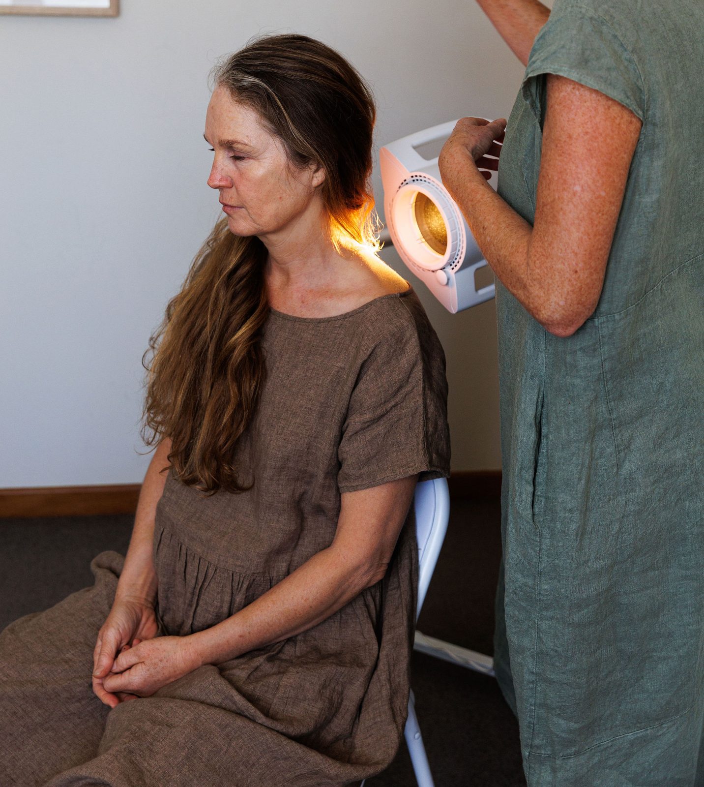 Caroline directing warm Bioptron light onto a seated client's neck and shoulder